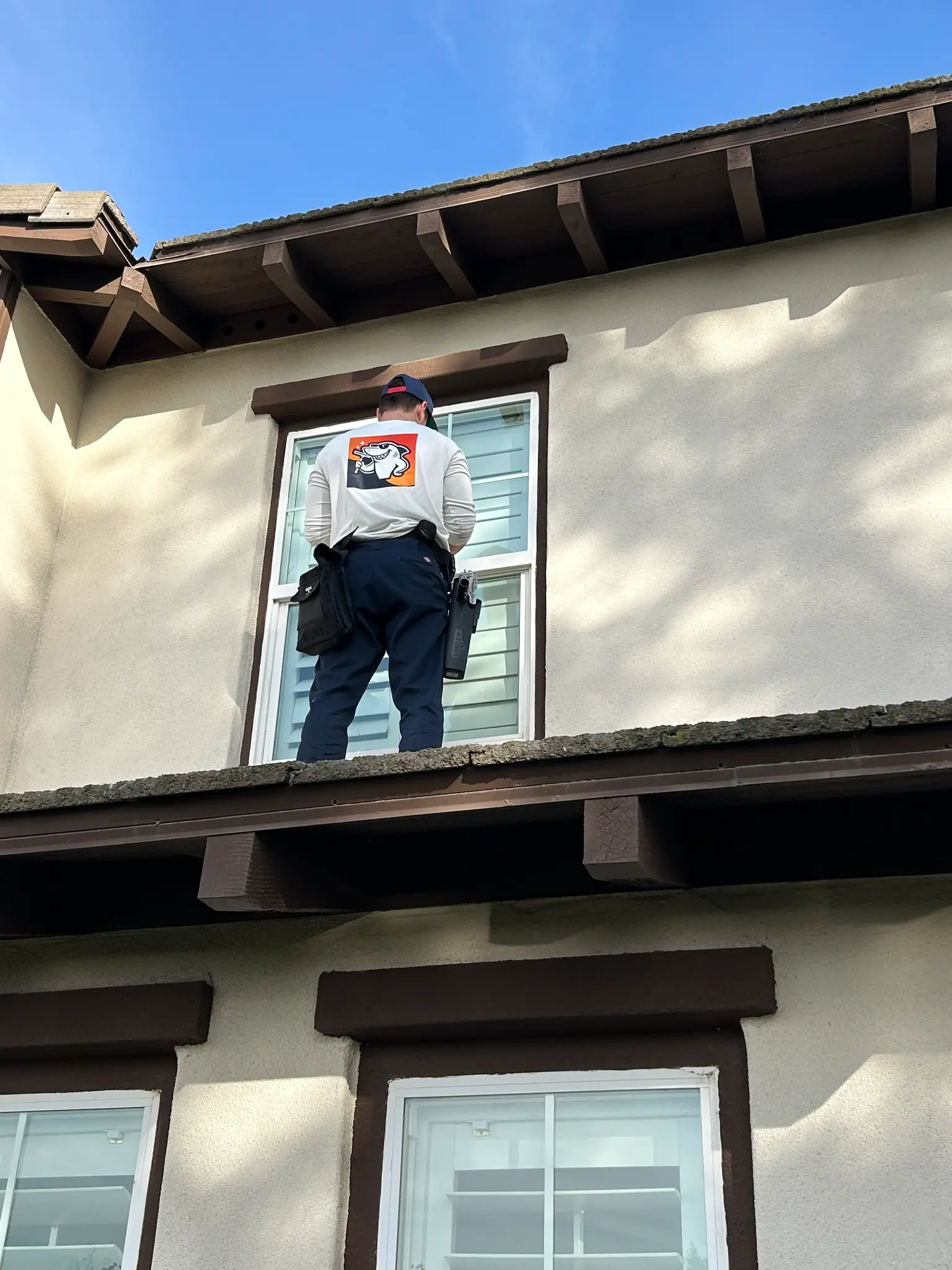 Squeegee Shark technician cleaning second-story windows on rooftop